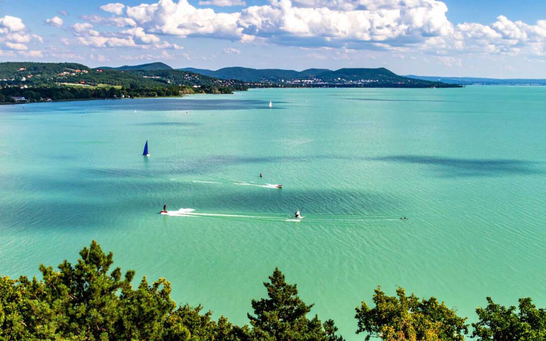 Urlaub in Ungarn aktiv Urlaub Balaton tuerkisblauer See mit Segelbooten und gruene Huegel im Hintergrund