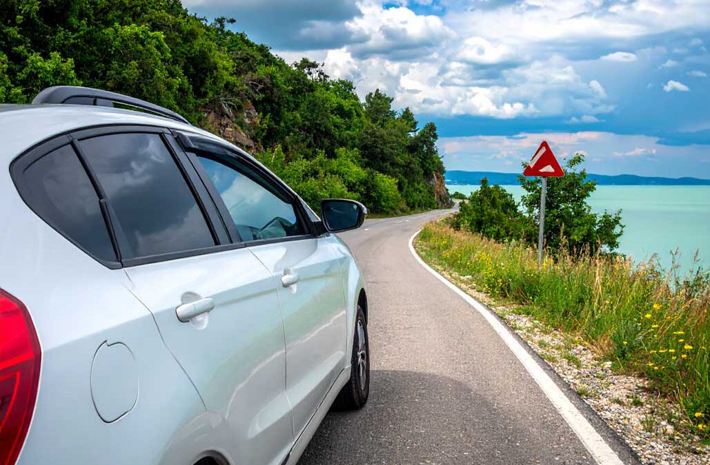 Balaton Anreise Tipps Auto auf kurviger Strasse am Seeufer mit gruener Landschaft und blauem Himmel