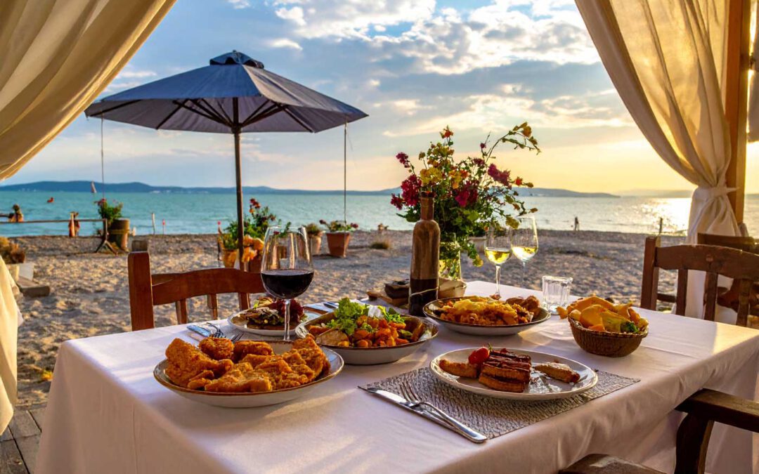 Essen und Trinken am Balaton gedeckter Tisch am Seeufer mit Wein und ungarischen Speisen bei Sonnenuntergang