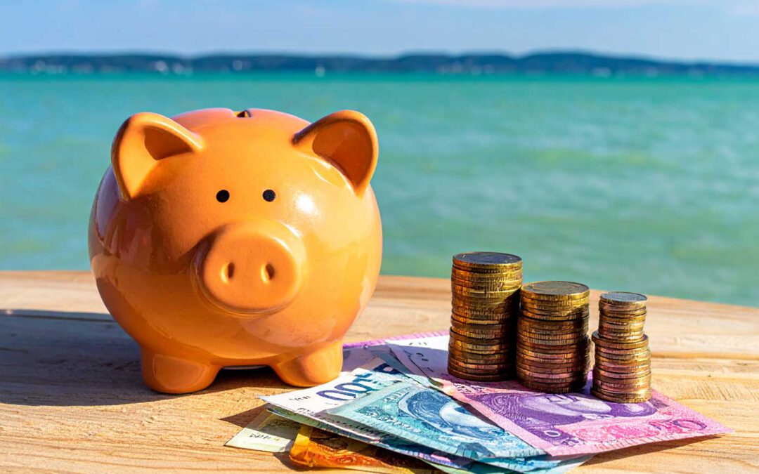 Kosten im Urlaub Ungarn Sparschwein mit Muenzen und Geldscheinen am Seeufer als Symbol fuer Urlaubsbudget